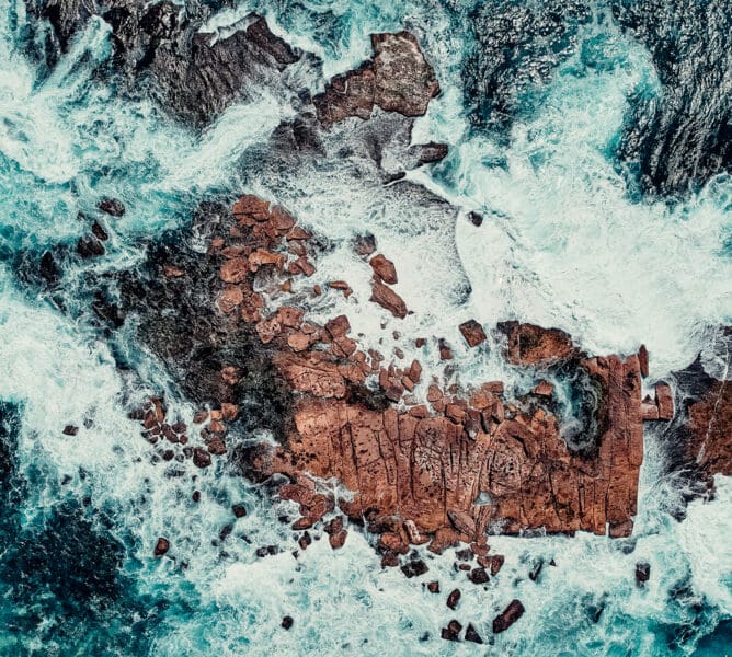 Aerial Drone View of Waves Crashing Onto Rocks In Blue Ocean