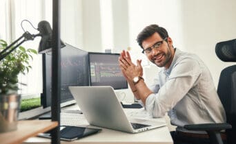 Young and successful. Happy bearded trader in formal wear and eyeglasses looking at camera and smiling while sitting in his modern office.