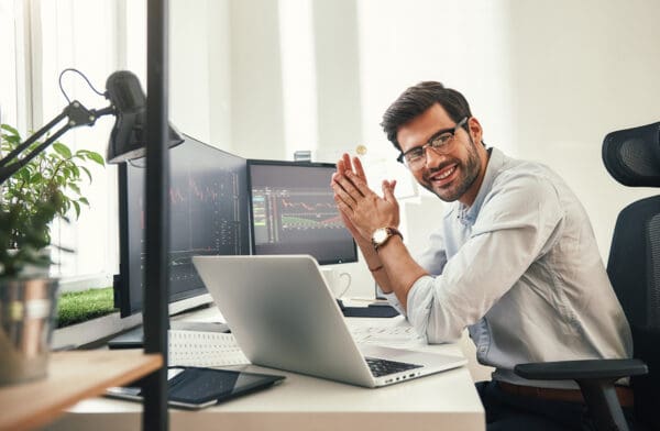 Young and successful. Happy bearded trader in formal wear and eyeglasses looking at camera and smiling while sitting in his modern office.