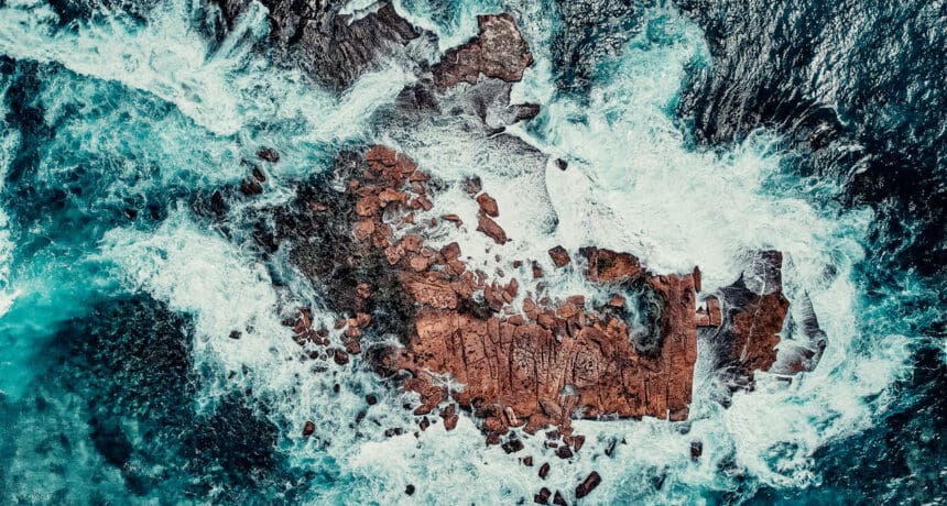 Aerial Drone View of Waves Crashing Onto Rocks In Blue Ocean